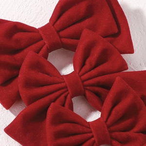 Detailed macro view of triple stacked large red velvet bow hair clips with soft matte texture