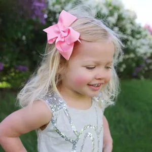 Detail of large pink grosgrain bow hair clip worn by a girl in a lush garden
