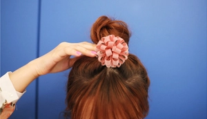 Élastique à cheveux rose en forme de fleur porté sur un chignon sur fond bleu