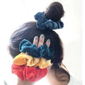 Detail of four velvet hair scrunchies in navy, green, yellow, and red on a model ponytail
