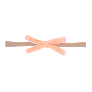 Détail du nœud en velours rose pêche sur un bandeau élastique pour bébé en nylon