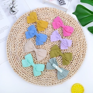 Set of 8 colorful cotton linen bow hair clips for girls arranged on a woven mat