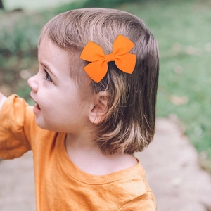 Bright orange grosgrain ribbon hair bow clip worn by a toddler in a sunny outdoor park