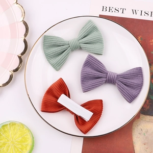 Three-piece corduroy bow hair clips in green, lilac, and red on a decorative tray