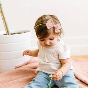 Infant light pink bow headband set on elastic nylon band worn by a toddler model