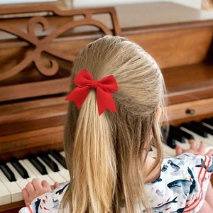 Bambina che indossa un grande fiocco di velluto rosso tra i capelli mentre suona il piano