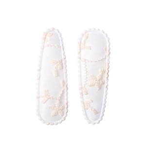 Detailed close-up of white fabric hair clips with floral embroidery and scalloped edges