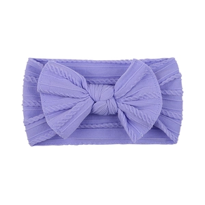 Close-up of a soft purple knitted baby headband featuring a large bow and cable pattern