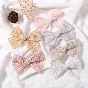 Flat lay of six lace bow hair clips in soft Morandi colors on white wrinkled fabric