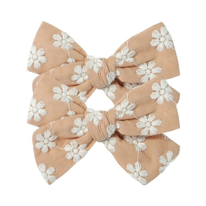 Detailed view of three light orange fabric hair clips with embroidered daisy patterns