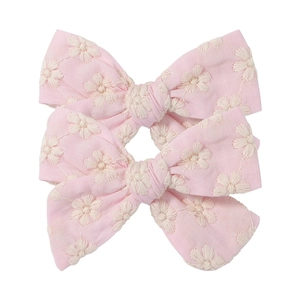 Macro detail of pink floral embroidery texture on fabric bow hair clips with white flowers