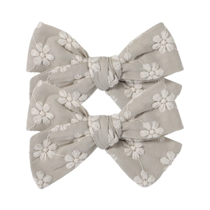 Detail shot of two grey fabric bow hair clips with delicate white daisy embroidery