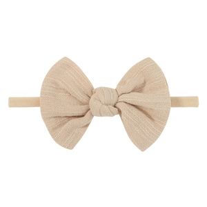 Detail of a beige cotton infant bow headband with textured weave and elastic nylon band