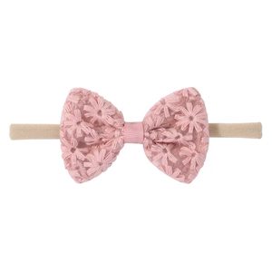 Détail du nœud en dentelle rose avec broderie marguerite sur un bandeau pour bébé
