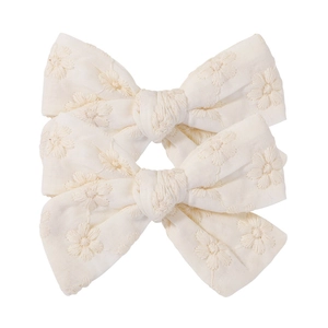 Detail of two cream floral embroidered cotton bow hair clips showing textured fabric craft