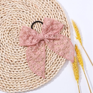 Close-up of pink lace bow hair tie with floral embroidery on a rustic straw mat