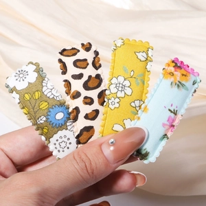Close-up of four floral and leopard print fabric BB hair clips held by hand on silk