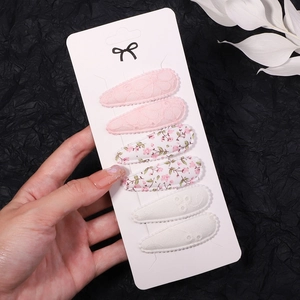 Detail showing set of six fabric floral hair clips on a white card display held by hand