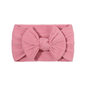 Detail of pink knitted baby headband featuring a large bow and elastic ribbed texture
