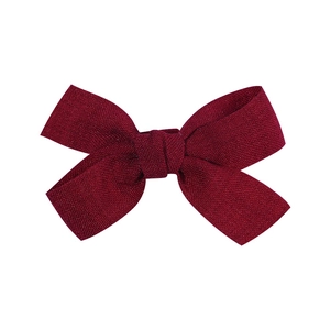 Detailed close-up of dark red fabric bow hair clip with fine shimmering texture