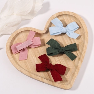 Close-up of four linen fabric baby bow hair clips in a heart-shaped wooden tray