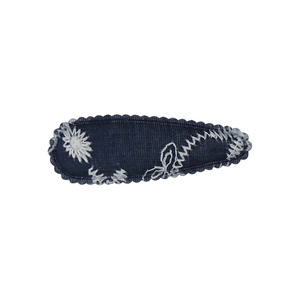 Detail of dark blue denim flower hair clip with white daisy embroidery and stitched edges