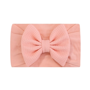 Détail du bandeau bébé rose pêche avec un grand nœud en maille gaufrée sur tissu lisse