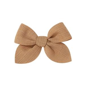 Detail of a brown fabric bow hair clip featuring a textured linen-cotton weave material
