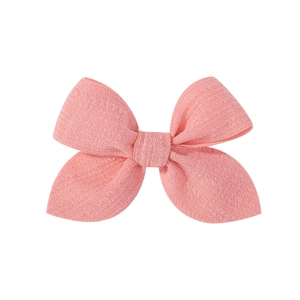 Close-up of peach pink fabric bow hair clip showing detailed weave texture and symmetry