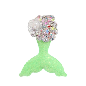 Détail de la pince à cheveux sirène avec tissu pailleté vert et perle sur un coquillage