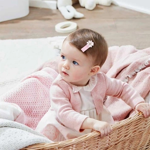 Neonata con molletta per capelli a forma di margherita rosa in un cesto di maglia