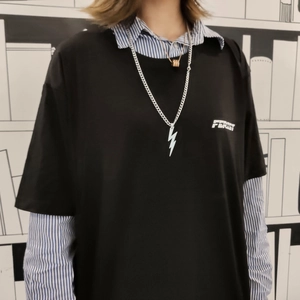 Détail du pendentif éclair argenté avec collier doré sur un t-shirt noir tendance