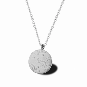 Détail macro du pendentif pièce argentée avec Saturne en relief et motifs de l'espace