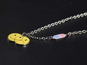 Detalle de collar de acero de titanio con cápsula de pastilla de colores y dijes smiley