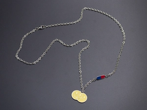 Detalle de cadena de acero plateada con colgante de carita sonriente y dije de cápsula