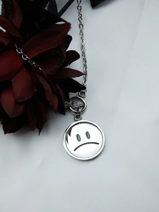 Close-up of silver titanium steel necklace featuring a rotating sad face pendant and OT buckle