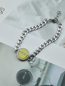 Detalle de pulsera de cadena plateada con colgante de cara sonriente amarilla esmaltada