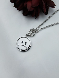 Close-up of polished silver spinning sad face pendant necklace with toggle clasp