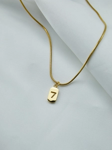Détail macro du collier pendentif chiffre 7 doré sur fond élégant en soie blanche