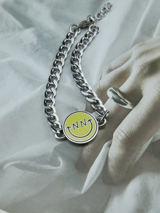 Primer plano de una pulsera de cadena gruesa plateada con colgante de esmalte amarillo sonriente