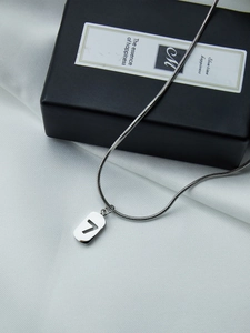 Gros plan d'un pendentif argenté rectangulaire numéro 7 avec chaîne en maille serpent