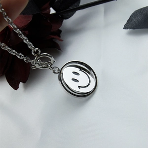 Minimalist stainless steel rotating smiley face necklace with OT clasp on white silk fabric