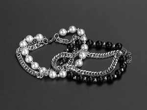 Detail of layered hip-hop bracelets featuring pearls and silver cuban chains on gray background