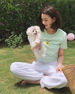 Detail of light green smile face t-shirt paired with white jogger pants on grass