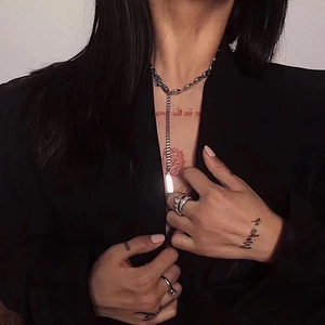Detail of silver titanium square pendant necklace and iced-out rings on a tattooed model