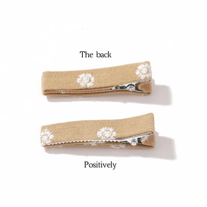 Pair of fabric hair clips with white daisy embroidery on light brown textured cloth
