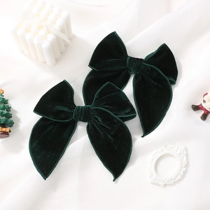 Detail of two dark green velvet bow hair clips on white silk with festive decorations