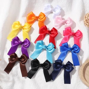 Flat lay of satin hair bow clips in eleven candy colors on a soft white texture background