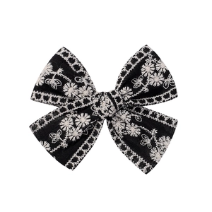 Détail d'un nœud à cheveux noir avec broderie de marguerites blanches et texture tissée