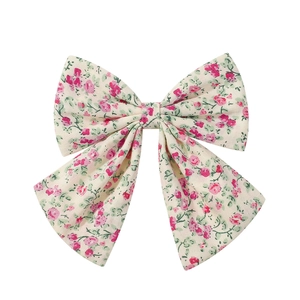 Detail of floral bow hair clip featuring delicate pink roses on cream fabric with long ribbons